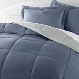 A bed with a blue comforter and matching pillowcases, accompanied by white pillows and a gray blanket edge.