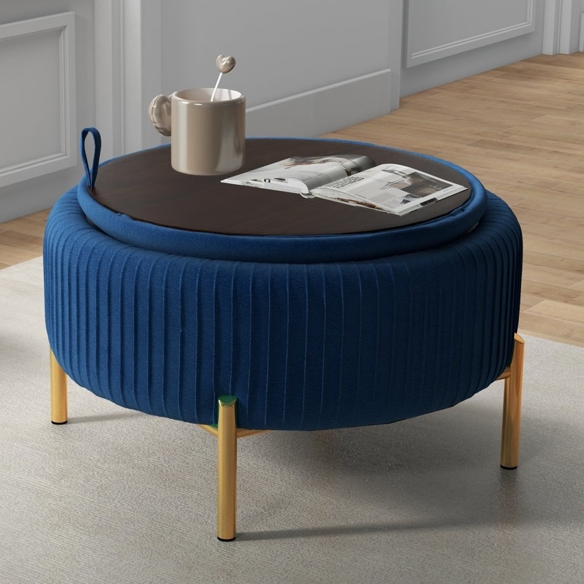 A round, blue upholstered ottoman with wooden legs and a removable wooden top is used as a coffee table, with a mug and an open magazine on it.