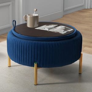 A round, blue upholstered ottoman with wooden legs and a removable wooden top is used as a coffee table, with a mug and an open magazine on it.