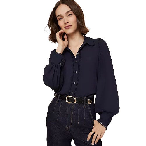 A woman is wearing a dark blue, long-sleeve blouse with a collar and button detailing, paired with high-waisted dark denim jeans and a black belt with a gold buckle.