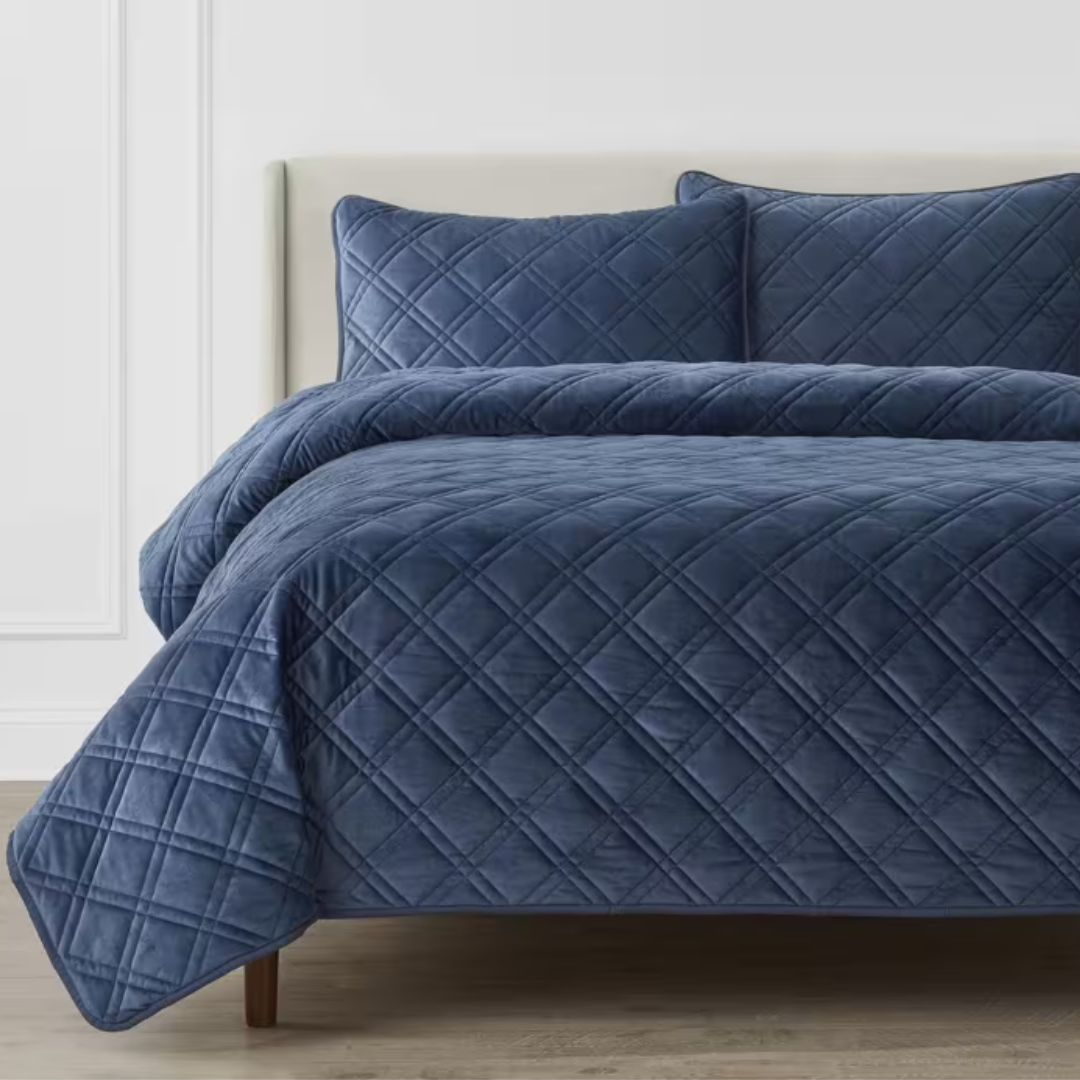 A navy blue quilted comforter and matching pillows on a bed.