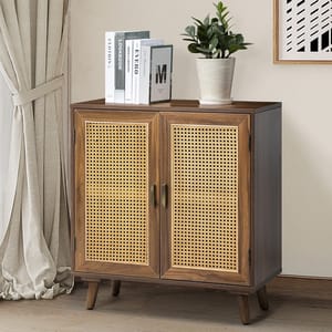 A small wooden cabinet with cane doors and tapered legs, featuring a potted plant and a few books on top. The cabinet is placed beside a light-colored curtain and a modern art piece on the wall.