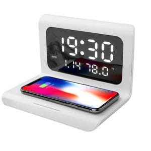 This is a white digital alarm clock featuring a large display and a built-in wireless charging pad for smartphones. The clock shows time, date, and temperature.