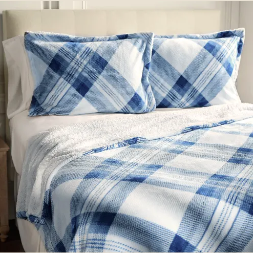 A bed is shown with a blue and white plaid blanket and matching pillowcases, set against a white headboard.