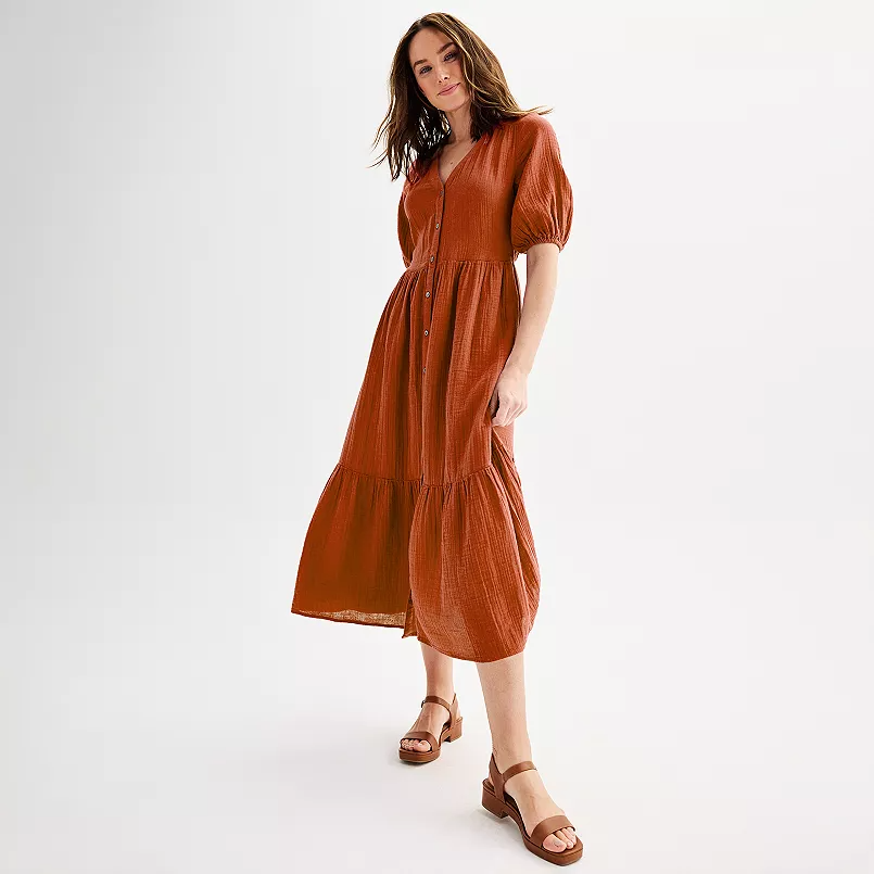 A woman is wearing a burnt orange midi dress with puff sleeves and tiered skirt, paired with brown sandals.