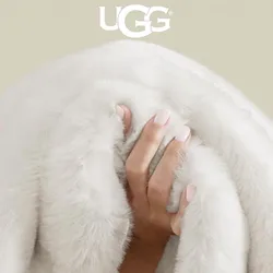 A hand grips a fluffy, white UGG blanket, conveying its softness and warmth.