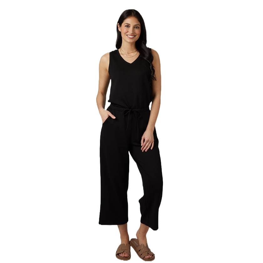 A woman wearing a black, sleeveless jumpsuit with a drawstring waist, paired with brown sandals.