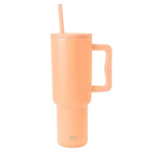 A tall, peach-colored travel mug with a handle, lid, and straw, featuring a small \“slm\“ logo near the base.