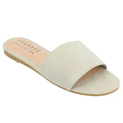 A light beige slide sandal from Journee Collection, featuring a wide suede strap and a flat sole.