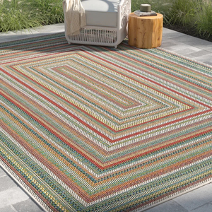 Outdoor patio setup featuring a multi-colored striped rug with a geometric pattern, a wicker chair with a blanket, and a small wooden stump table.