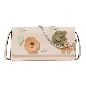 A beige Kate Spade New York handbag adorned with 3D floral and leaf appliqués. It features a chain strap and floral accents in peach and olive tones.