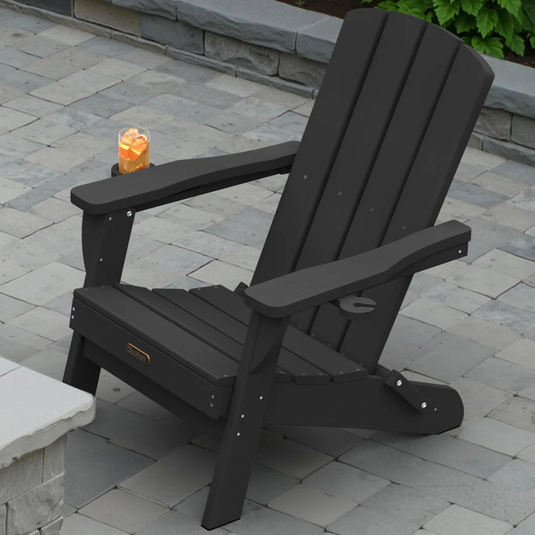 Black Adirondack chair with a drink placed on its armrest, set on a stone-tiled patio.