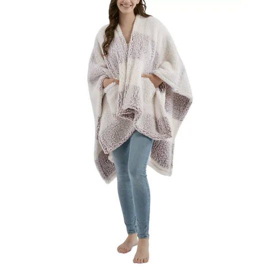 A person is wearing a cozy, sherpa-textured poncho-style wrap with a checkered pattern in soft colors over skinny blue jeans.