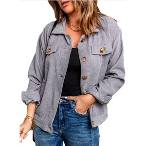 Gray corduroy shacket featuring a button-up front, chest pockets with button closures, long sleeves, and a relaxed fit. Worn over a black top and paired with blue jeans.