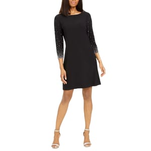 Black dress with three-quarter sleeves featuring pearl embellishments and paired with white strappy heels.