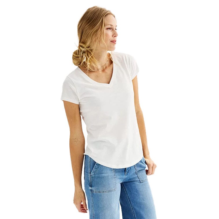 A woman wearing a white V-neck T-shirt and light blue jeans. Her hair is styled in a loose bun, and she is looking to the side.