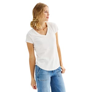 A woman wearing a white V-neck T-shirt and light blue jeans. Her hair is styled in a loose bun, and she is looking to the side.