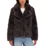 A woman is wearing a dark gray, fluffy faux fur jacket over a white shirt, paired with light blue jeans.