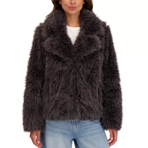 A woman is wearing a dark gray, fluffy faux fur jacket over a white shirt, paired with light blue jeans.