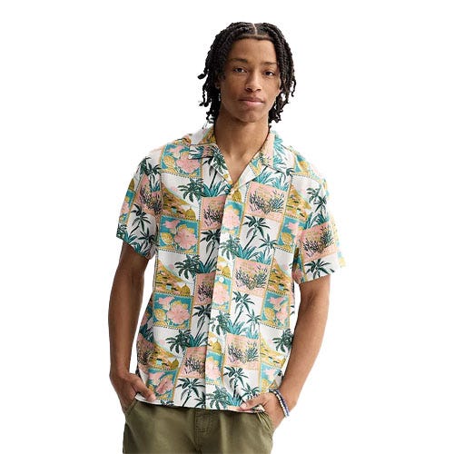 A person wearing a short-sleeve button-up shirt featuring a vibrant tropical print with palm trees and florals, paired with olive green pants.