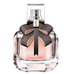 A perfume bottle with a clear, elegantly designed container features a black and beige bow around the neck, bearing a gold emblem with the YSL logo.