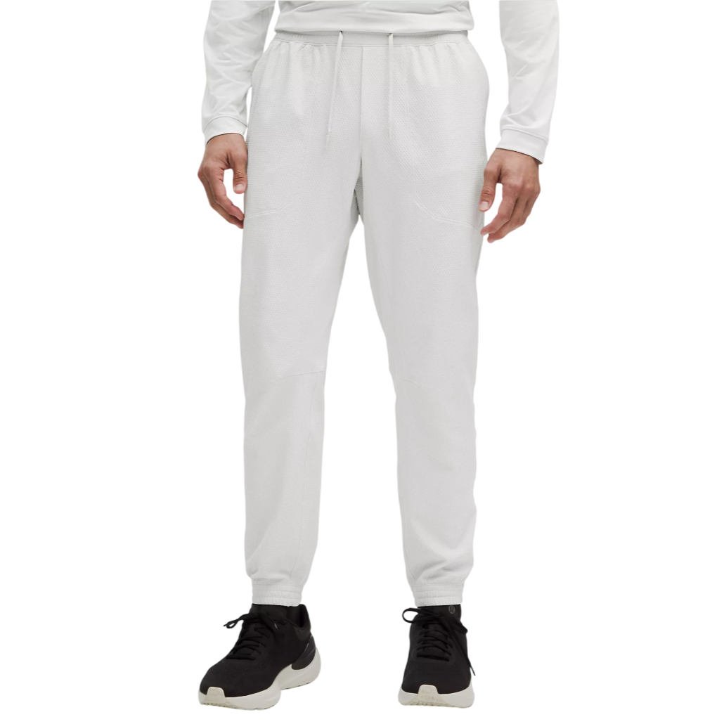 A person is wearing white joggers with a drawstring waist and ankle cuffs, paired with black athletic shoes. The outfit includes a long-sleeve shirt.
