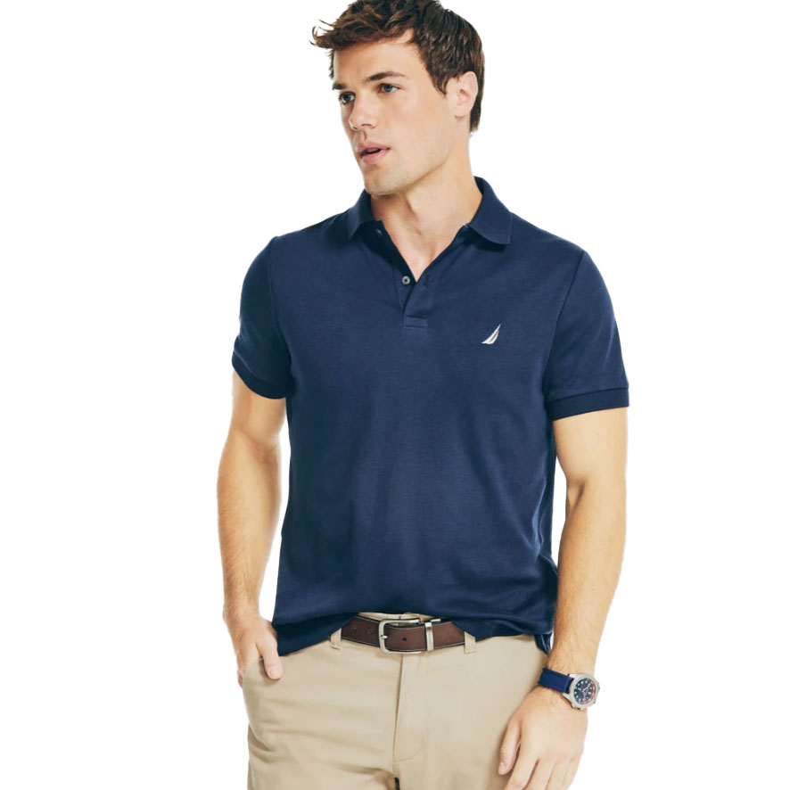 A man is wearing a navy blue polo shirt with a small sailboat logo on the chest, paired with khaki pants and a brown belt. He has a navy watch on his wrist.