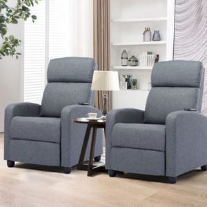 Set of two gray fabric massage recliners with cushioned high backs and armrests, positioned in a living room setting with a small round side table and lamp between them.