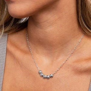 A woman wearing a silver necklace with five polished round beads on a delicate chain.