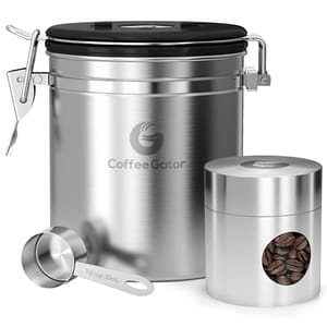 A stainless steel coffee storage set consisting of a larger canister with a clasp and seal lid and a smaller container, both with the Coffee Gator logo, plus a measuring scoop.