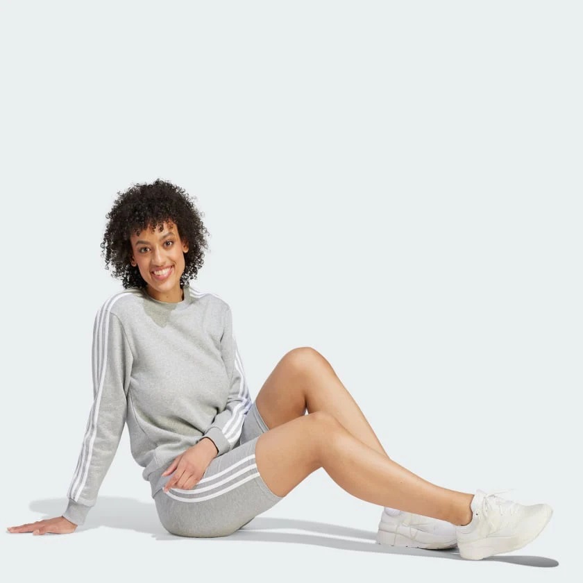 Woman in a grey sweatshirt and shorts with white sneakers sitting on a light background.