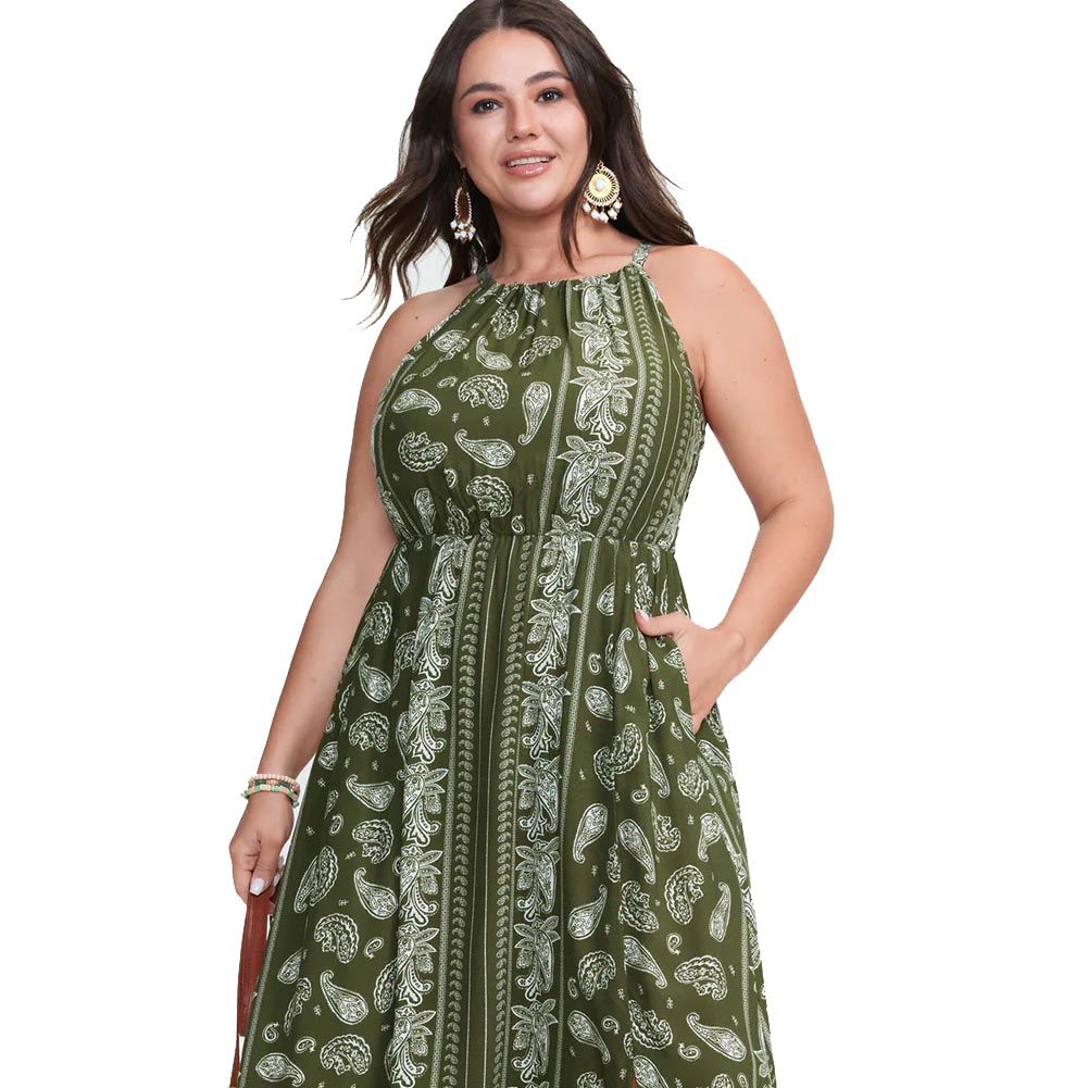 A woman in a sleeveless, green paisley-patterned dress with pockets and halter neckline, accessorized with large earrings and bracelets.