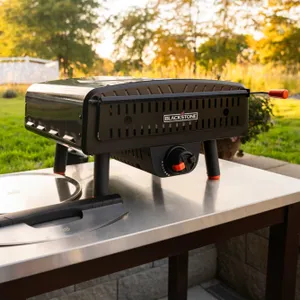 A portable Blackstone gas griddle on an outdoor table with a spatula beside it.