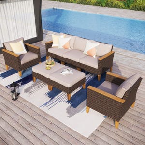 Outdoor seating set with a wicker sofa, two armchairs, and two ottomans, all featuring wooden legs and beige cushions. The setup includes a decorative rug, pillows, and a poolside view.