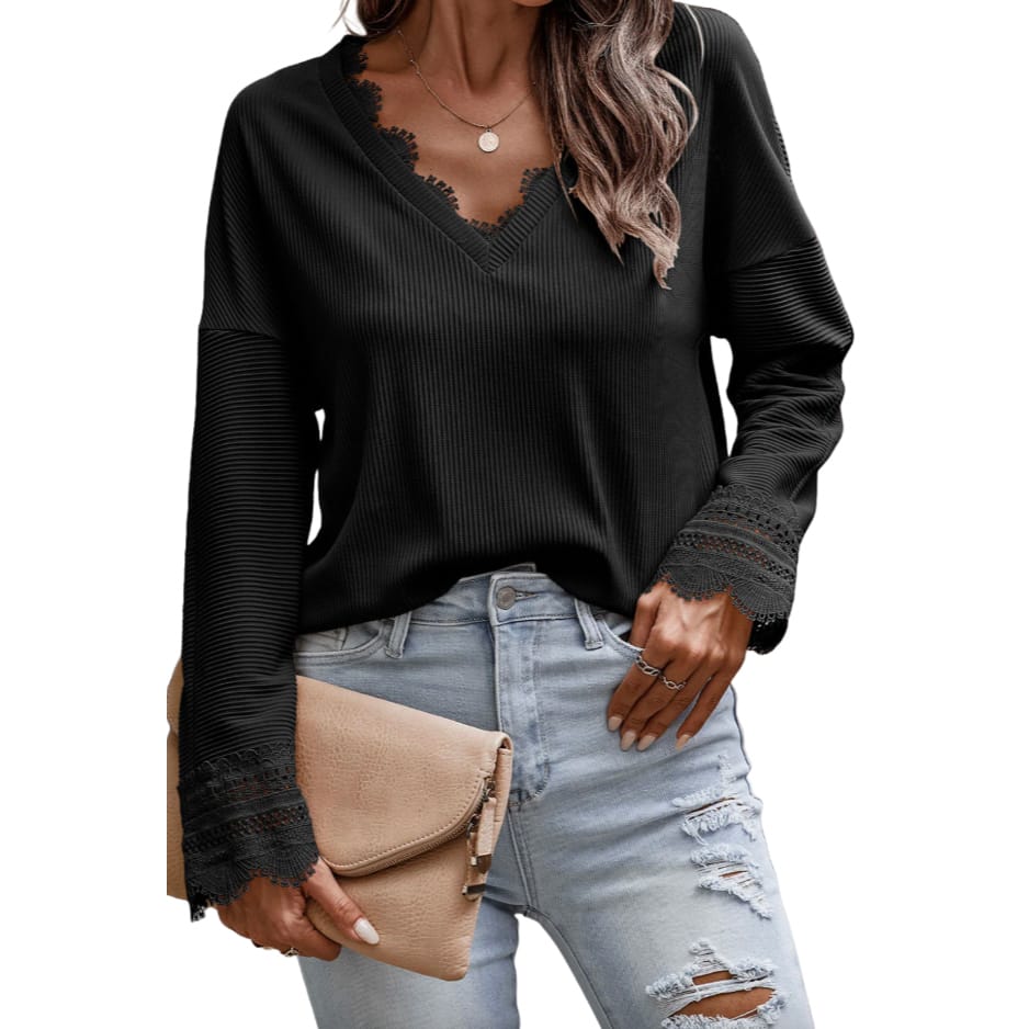 A black, long-sleeve, ribbed top with lace trim detailing along the V-neckline and cuffs, paired with light blue distressed jeans and a beige clutch.