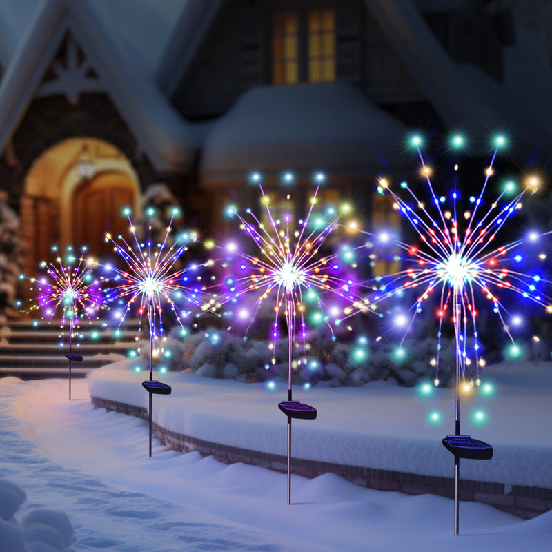 Solar-powered LED garden lights shaped like fireworks display colorful lights outdoors in a snowy setting, lining a pathway to a house.