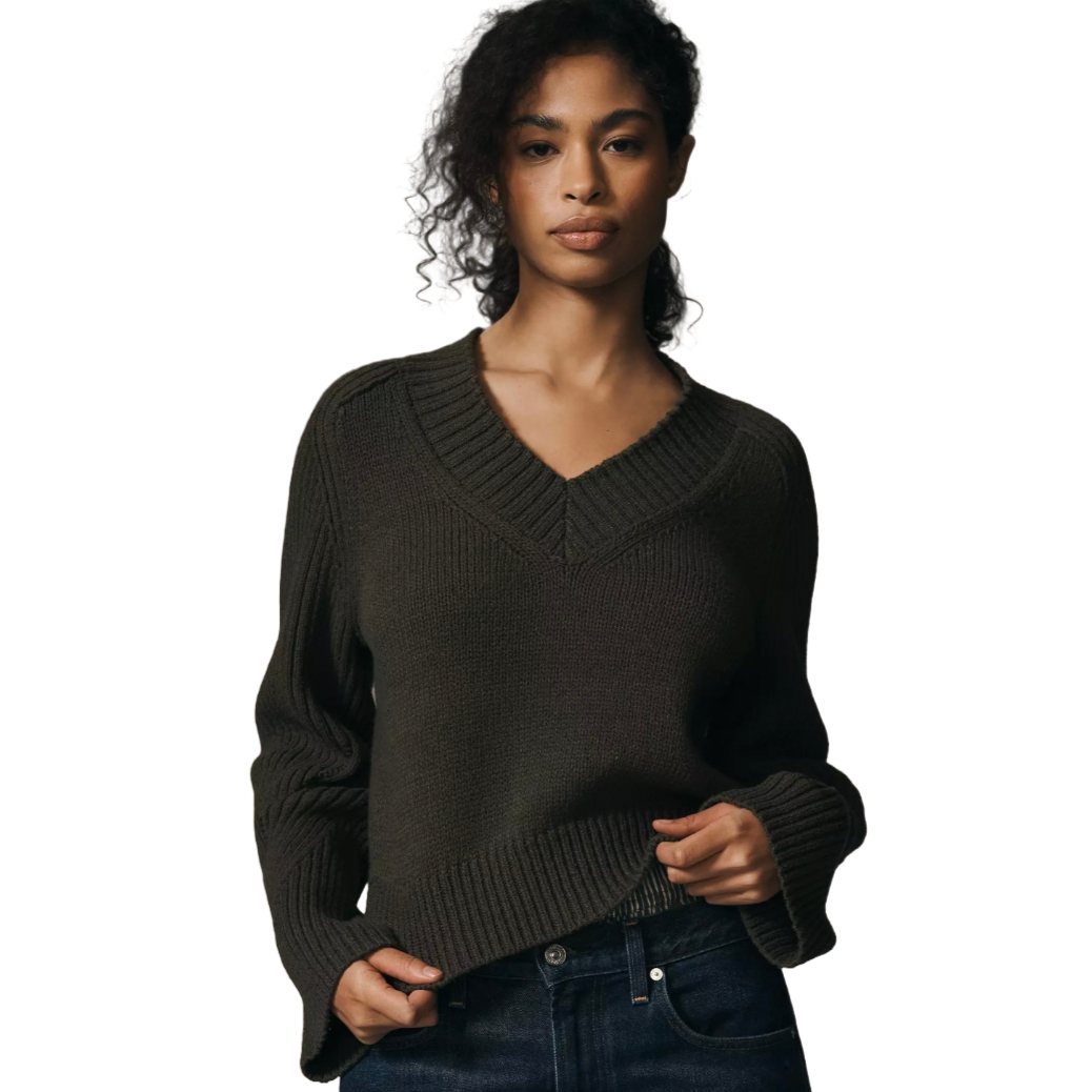 Dark green V-neck sweater with ribbed detailing along the neckline, cuffs, and hem, paired with dark denim jeans.