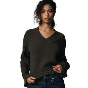 Dark green V-neck sweater with ribbed detailing along the neckline, cuffs, and hem, paired with dark denim jeans.
