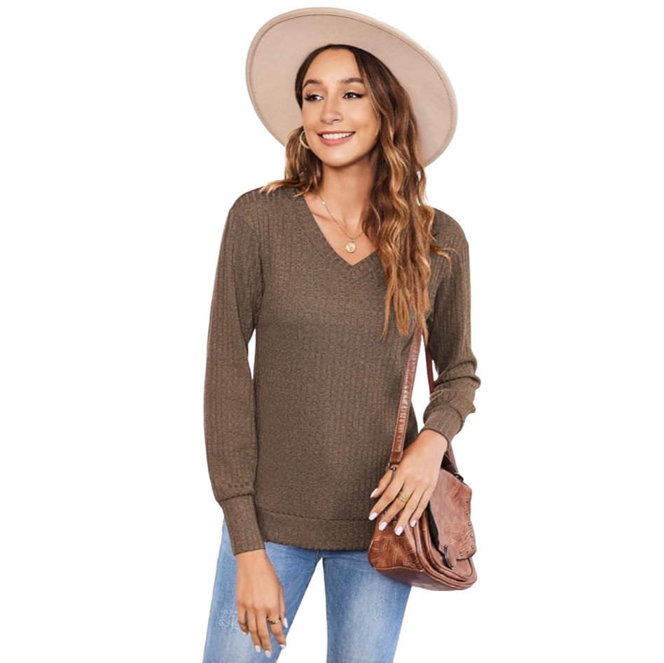 A brown V-neck sweater with long sleeves and ribbed texture, paired with light blue jeans. The outfit is complemented by a wide-brimmed hat, a brown crossbody bag, and a simple necklace.