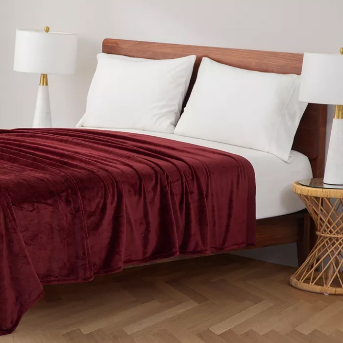 Wooden bed with white bedding and maroon velvet blanket, flanked by two white and gold table lamps.