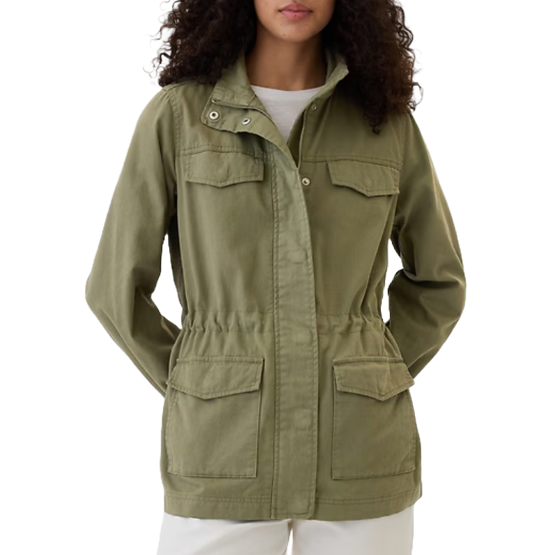 Olive green utility jacket with front zipper and snap closures, two chest pockets with flaps, and two waist pockets. It features a drawstring waist for a tailored fit and is paired with white pants.