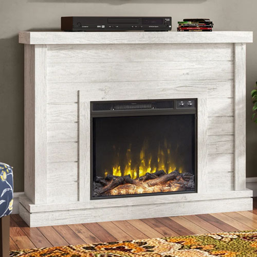 White wooden electric fireplace with a realistic flame effect, topped with electronic equipment, on a hardwood floor with a patterned rug nearby.