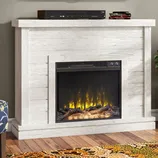 White wooden electric fireplace with a realistic flame effect, topped with electronic equipment, on a hardwood floor with a patterned rug nearby.