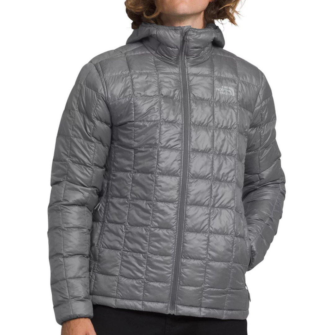 The North Face ThermoBall Puffer Jacket is a lightweight, gray, hooded jacket with a quilted design. It features a full-length front zipper and side pockets, providing both comfort and warmth.