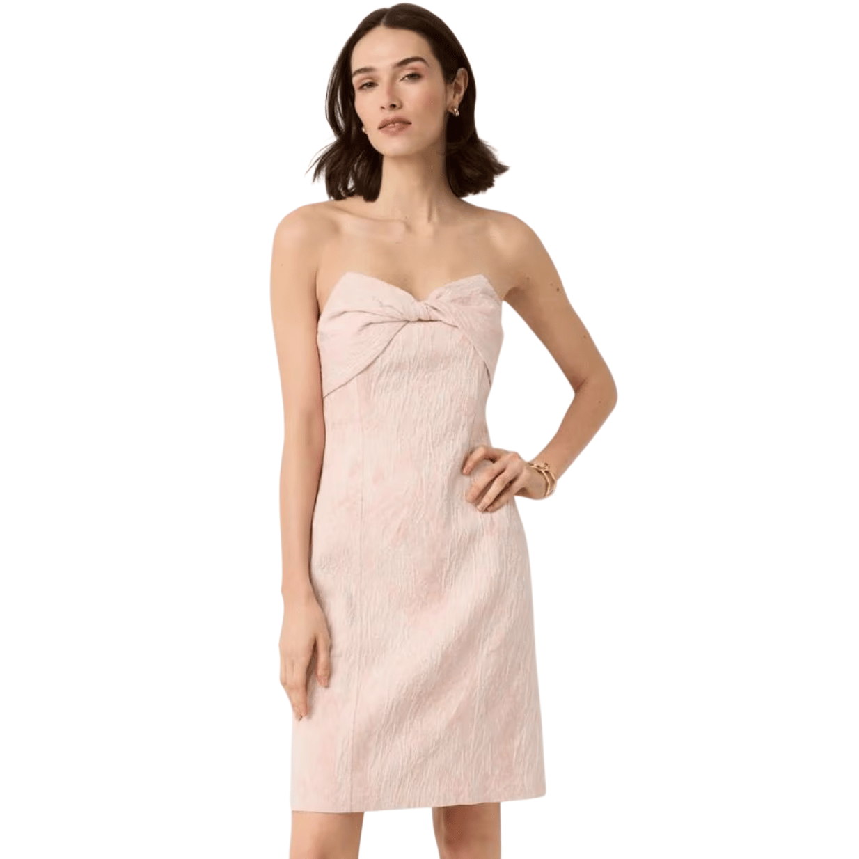 Strapless pink textured knee-length dress with a knotted detail at the bust, worn by a woman with short dark hair; paired with hoop earrings and a bracelet.