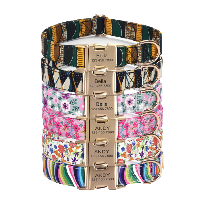 A stack of colorful pet collars with various patterns, featuring nameplates engraved with \“Bella\“ or \“Andy\“ and a phone number.