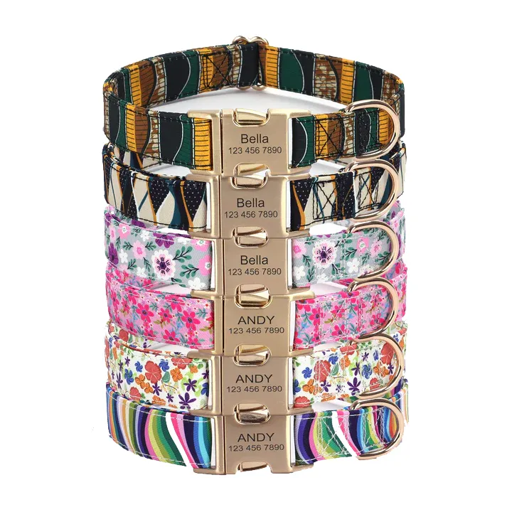 A stack of colorful pet collars with various patterns, featuring nameplates engraved with \“Bella\“ or \“Andy\“ and a phone number.