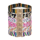 A stack of colorful pet collars with various patterns, featuring nameplates engraved with \“Bella\“ or \“Andy\“ and a phone number.