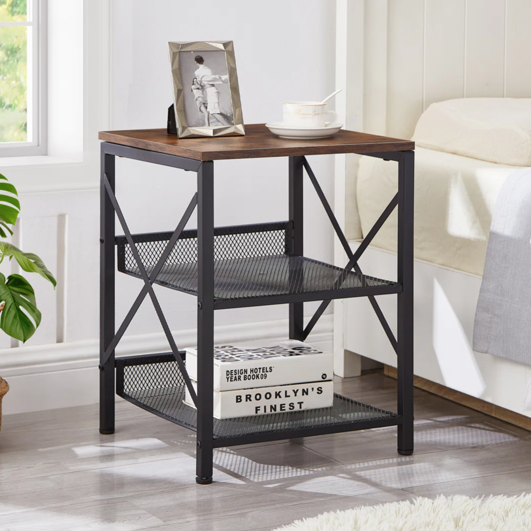 A modern nightstand with a wood top and black metal frame, featuring two mesh storage shelves. A framed photo, a teacup, and decorative books are on display.