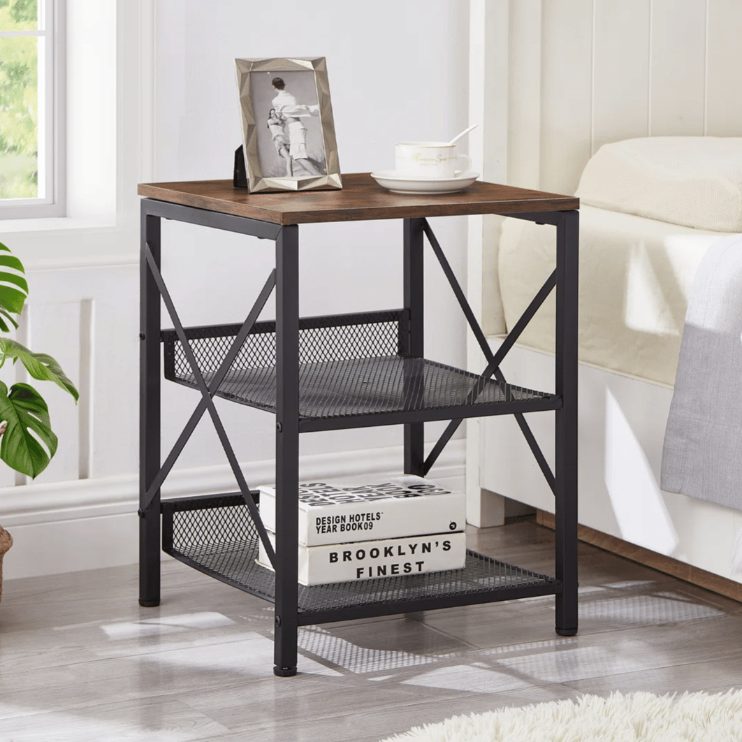 A modern nightstand with a wood top and black metal frame, featuring two mesh storage shelves. A framed photo, a teacup, and decorative books are on display.